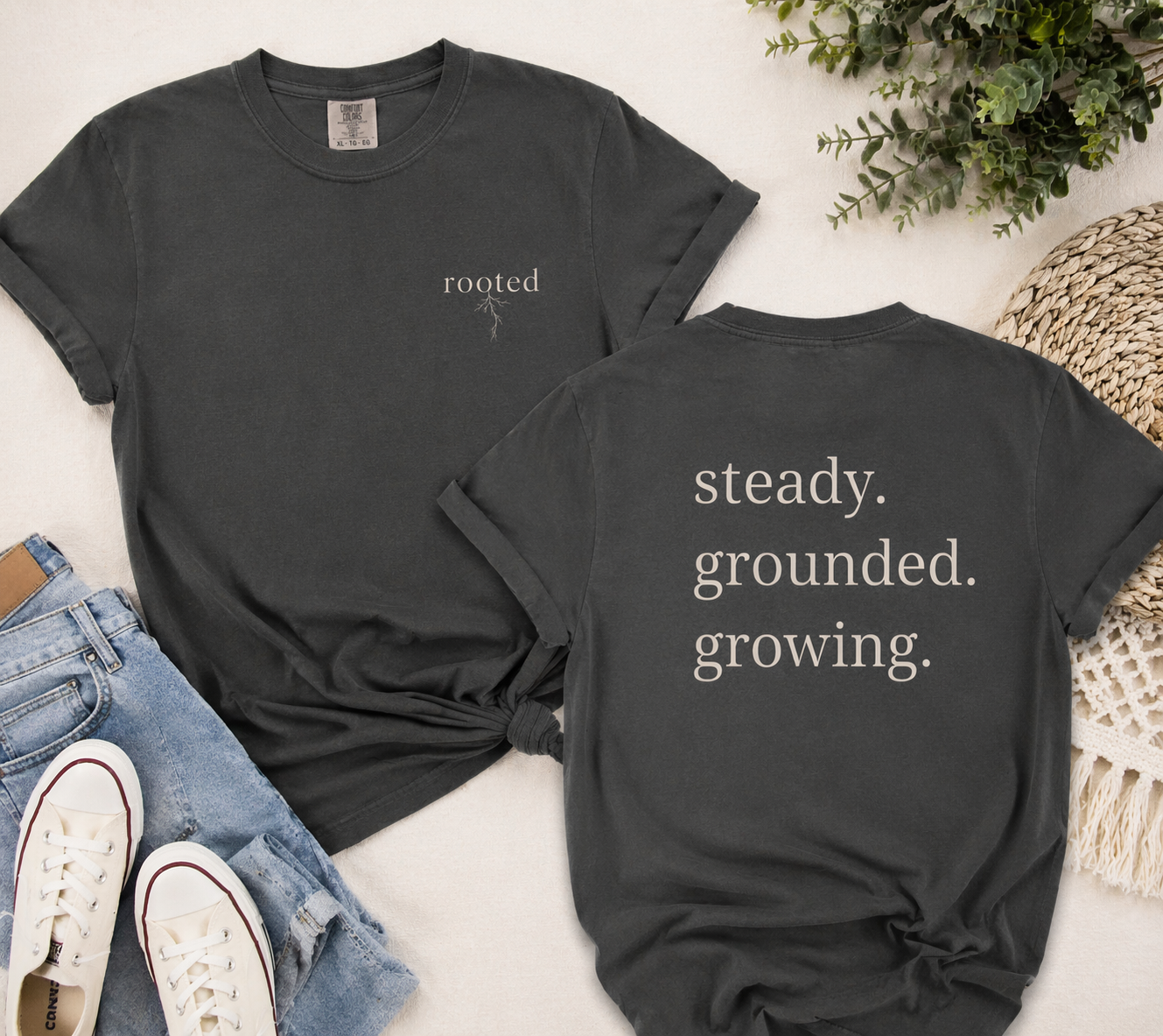 Black dark grey with 'rooted' on the front and 'steady. grounded. growing.' on the back, displayed with jeans and sneakers.