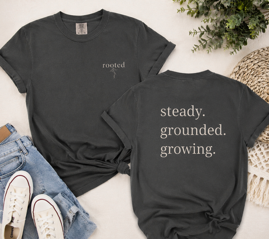 Black dark grey with 'rooted' on the front and 'steady. grounded. growing.' on the back, displayed with jeans and sneakers.